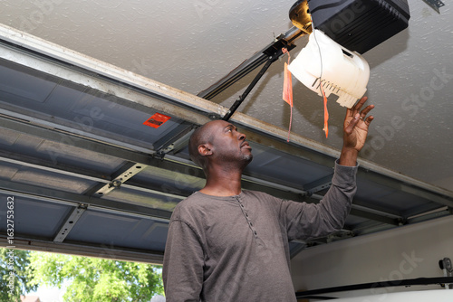 A portrait of a black African-American man changing a lightbulb in a overhead garage door opener 