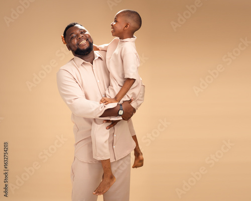 Obraz na plátne In warm studio light, an African father embraces his young son in matching beige