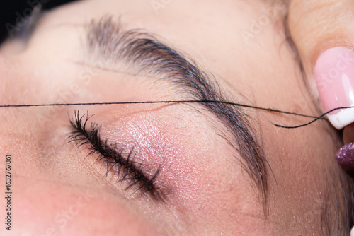 An unrecognizable woman waxing a client's eyebrow with white thread inside a beauty salon in Neiva, Huila, Colombia. Handmade and waxing concept