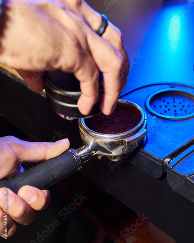 Close-up of a barista preparing to tamp freshly ground coffee in a portafilter, highlighting the espresso-making process