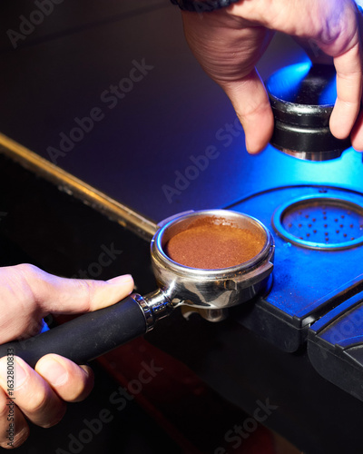 Close-up of a portafilter with tamped coffee grounds, ready for brewing, placed on a professional barista workstation
