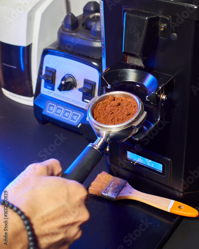 Close-up of a barista grinding fresh coffee into a portafilter using a professional espresso grinder, with bar tools in the background.