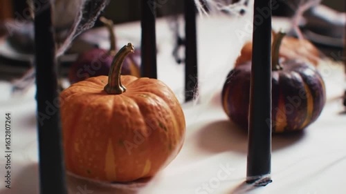 Halloween table with pumpkins, black candles, and spiderweb decor in a dark, elegant setting.
