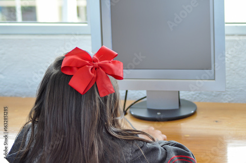 Young girl with red bow using computer in school classroom
