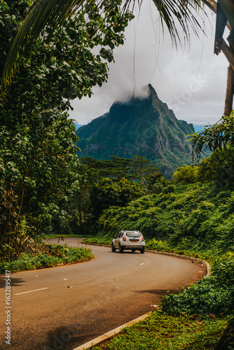 Scenic road trip through the lush jungle of Moorea Island, French Polynesia, with a view of Mount Rotui in the background partially covered by clouds