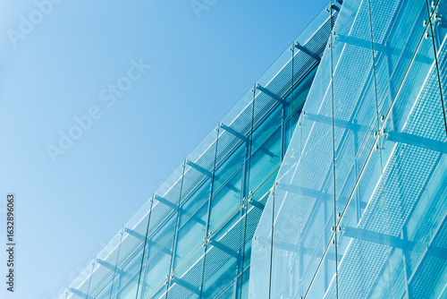 Contemporary architectural structure featuring a blue glass facade with metal framework under clear sky. Suitable for illustrating modern architecture, construction, and urban design concepts.