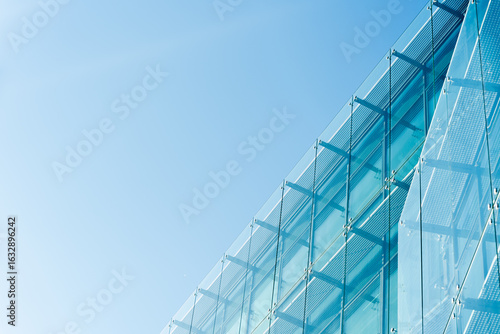 Contemporary architecture featuring a glass facade with metal framework under a bright blue sky. Suitable for illustrating urban design, construction, or architectural innovation concepts.