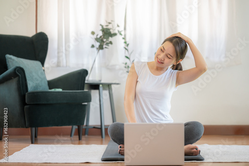 Happy smiling Asian woman doing neck stretching watching online class from laptop at home in living room 