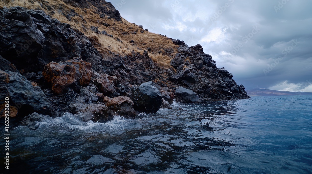 Obraz premium Waves crash against a rocky, grassy coastline under clouds.