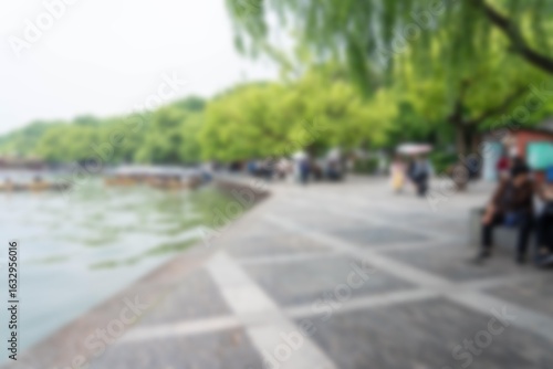 Wallpaper Mural A blurred view of a waterfront park in Hangzhou, China, with boats on the water and people walking along a stone path. Torontodigital.ca