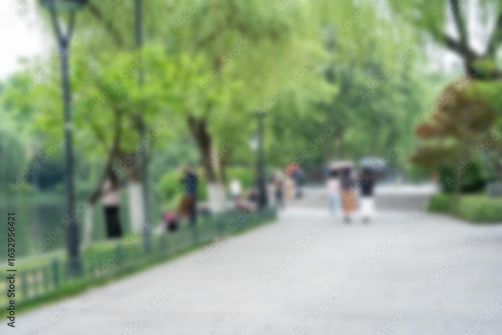 Obraz premium A blurred image of a pathway in a park with trees and people walking by.