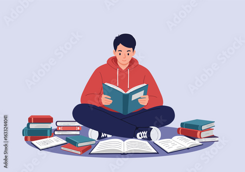 A studious young man sits cross-legged on the floor, deeply engrossed in reading a book among many scattered textbooks and notes.