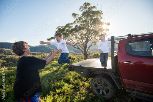 Happy kids jumping off back of ute to teenage boy in the Australian bush