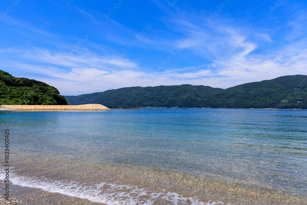 Obraz premium 愛媛県伊方町、砂浜から望むムーンビーチ井野浦と防波堤、遠くに見える風車の夏景色