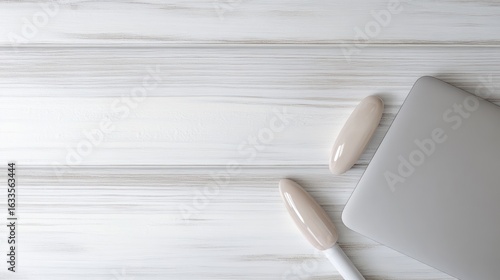 Light gray laptop and two light beige objects on a white wooden surface