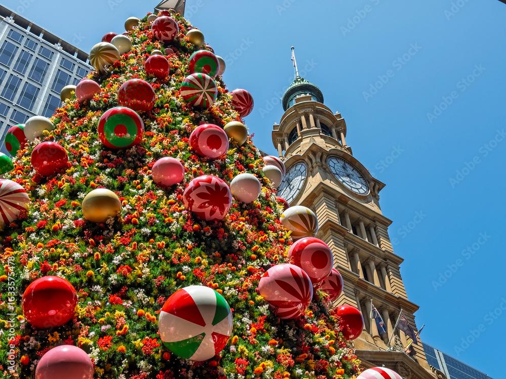 Obraz premium Giant Christmas tree decorated with colorful ornaments and flowers standing in Sydney near clock tower