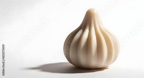 A single modak dessert with a pleated design sitting on a white surface casting a soft shadow to the left