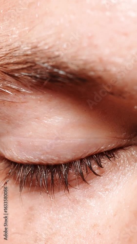 A close up of a person's eye with a blurry background. The eye is slightly closed and the eyelashes are visible