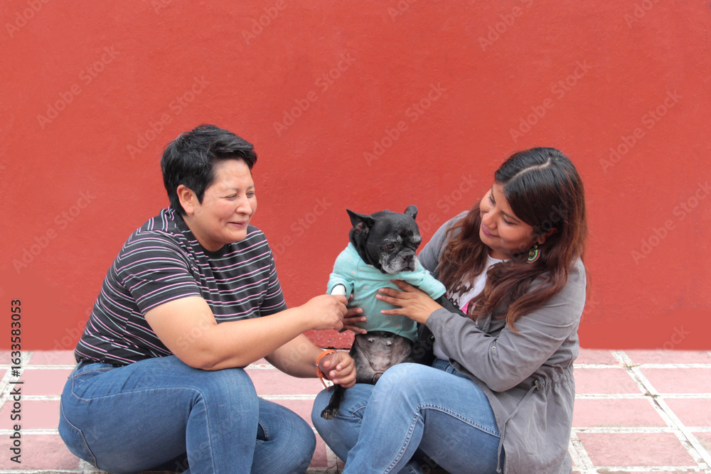 Obraz premium Couple of two brunette Latina lesbians show their love for the dog that is their pet and part of their family