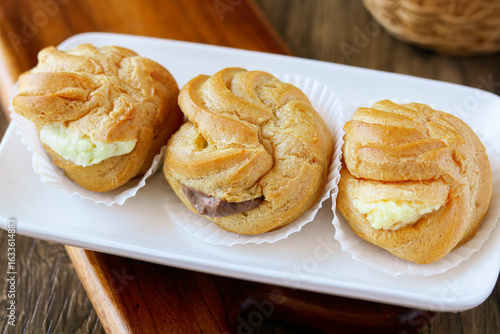 Obraz na plátně Three freshly baked Kue Sus (Choux Pastries or Cream Puffs) neatly arranged on a  white rectangular plate