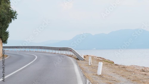 Wallpaper Mural Winding asphalt road along the coast of Aegina Island, Greece. White centerline, stone wall, metal guardrail, calm sea, hazy mountains, small boat in distance. No people. Authentic Greece. Torontodigital.ca