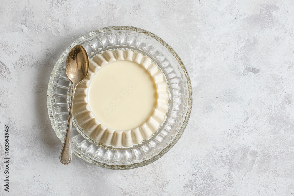Fototapeta premium A panna cotta dessert in a glass dish with a spoon on a textured surface