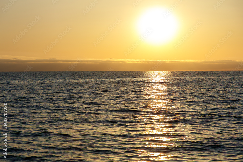 Obraz premium The sun is setting over the ocean, casting a warm glow on the water