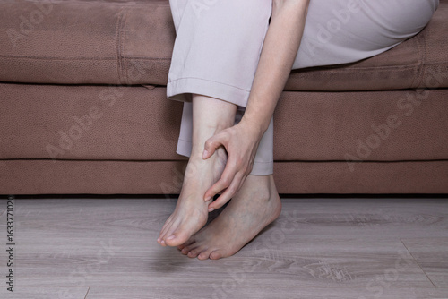 Φωτογραφία Close up of woman massaging aching foot while sitting on sofa at home