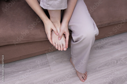 Foto Woman touching aching foot while sitting on sofa indoors