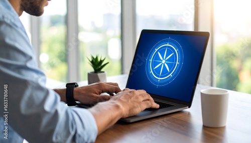 Man types on laptop displaying compass rose, working from home office
