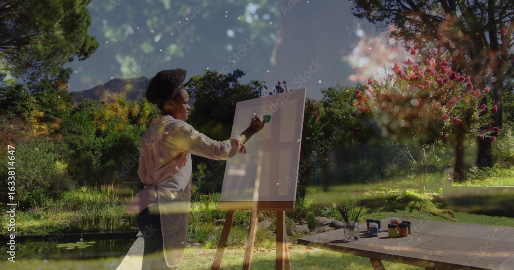Naklejka premium Painting African American woman applying green paint on canvas in lush garden, with lily pond