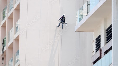 A professional worker paints the tall exterior wall of a building with his shadow on a facade
