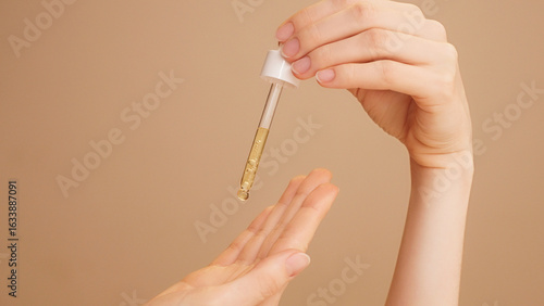 Photos Close-up of female hands on isolated beige background holding dropper, anti-aging facial serum, booster dripping on palm