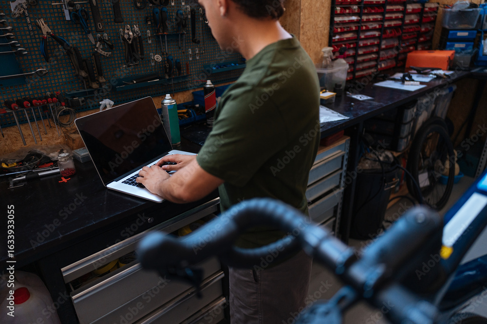 Fototapeta premium Bicycle mechanic using laptop in repair shop, searching spare parts