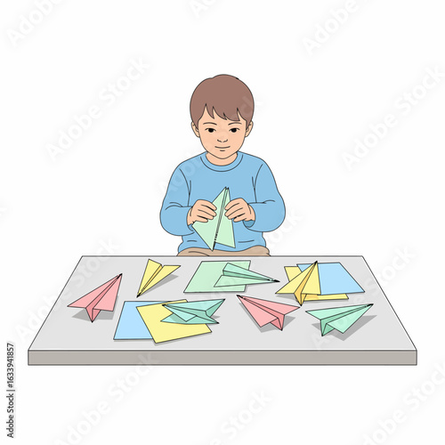 A young boy in a blue sweater sits at a table folding a green paper airplane among many colorful creations.