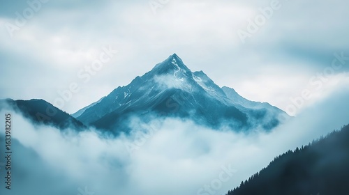 Majestic mountain peak piercing through ethereal clouds a serene landscape of cool tones evoking peace and wonder aerial