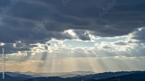Cloudy sky with sun rays over rolling hills creating a scenic, peaceful landscape