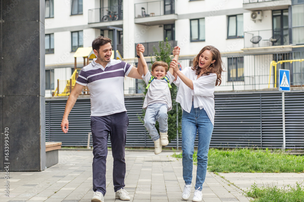 Fototapeta premium Happy parents swinging son while walking outside. Back to school