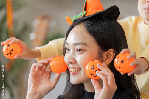 Halloween Joy. A woman poses with pumpkin toys while her son playfully interacts.