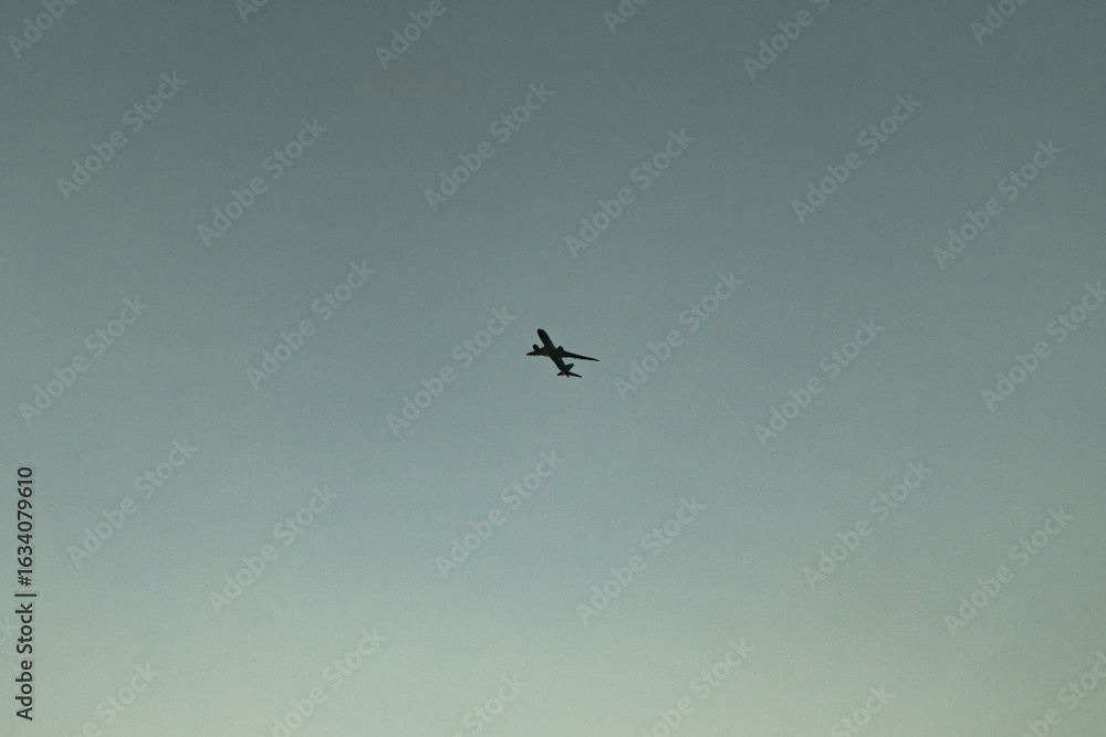 Obraz premium Silhouette of Passenger Jet Flying Across a Moody Sky