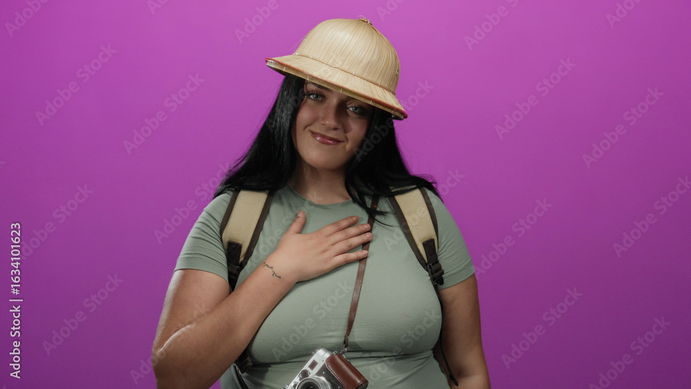 Φωτογραφία Woman smiling wearing pith helmet and backpack standing against a pink wall background with a camera hanging, embodying travel and adventure with joy and curiosity