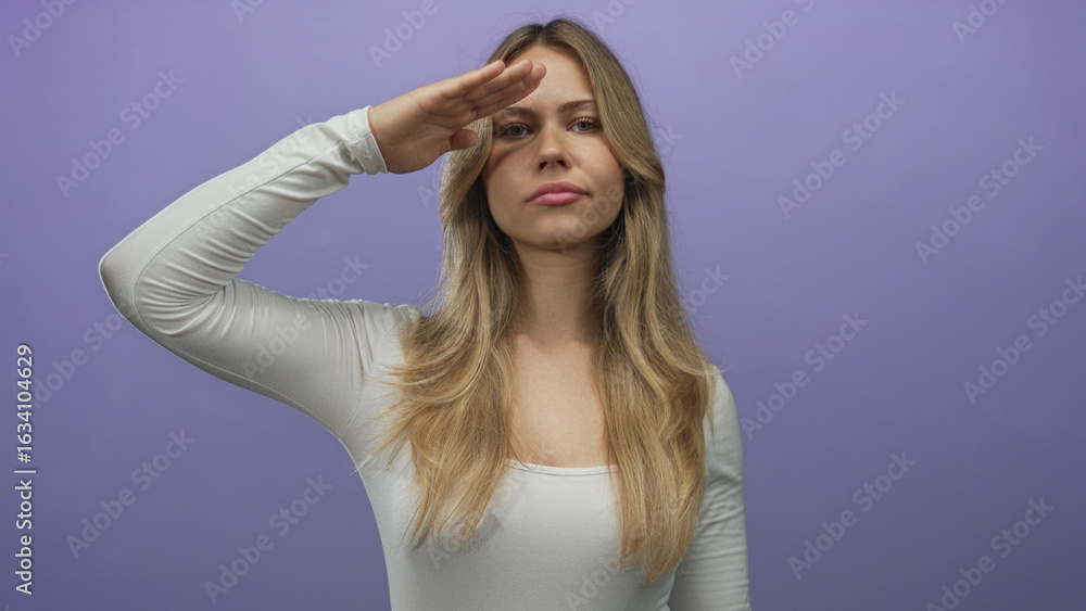 Fototapeta premium Woman long blonde hair lifts right hand to forehead in salute in studio; respect duty discipline honor.