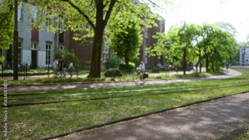 Blurred park scene with bokeh effect featuring people walking and cycling under lush green trees on a sunny day creating a peaceful urban atmosphere. Blurred park scene with bokeh effect featuring people walking and cycling under lush green trees on a sunny day creating a peaceful urban atmosphere.