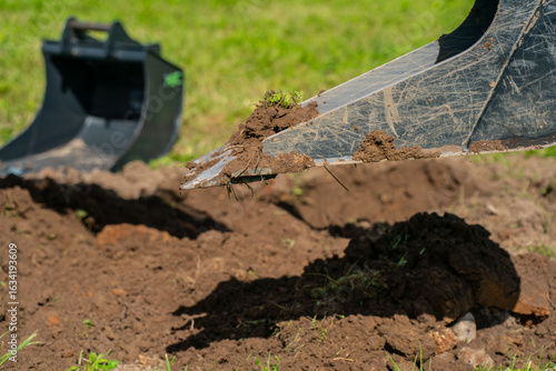 Wallpaper Mural Excavator bucket lifting soil during trenching work on construction site with loose earth and grass, showcasing precision digging for utilities or landscaping applications Torontodigital.ca