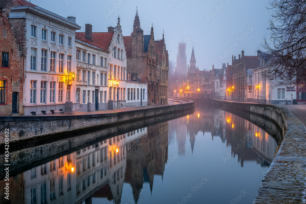 Fototapeta premium A foggy canal in the early morning in Bruges, with still water and historic buildings on both sides, moody atmosphere