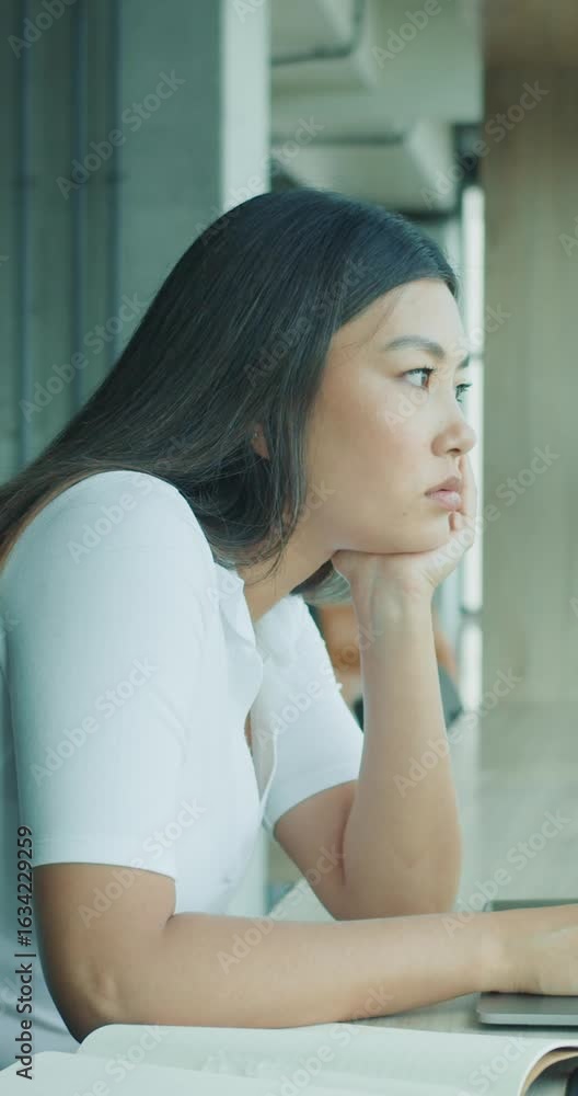 A pensive and contemplative young woman is sitting at her desk in a modern office setting A pensive and contemplative young woman is sitting at her desk in a modern office setting