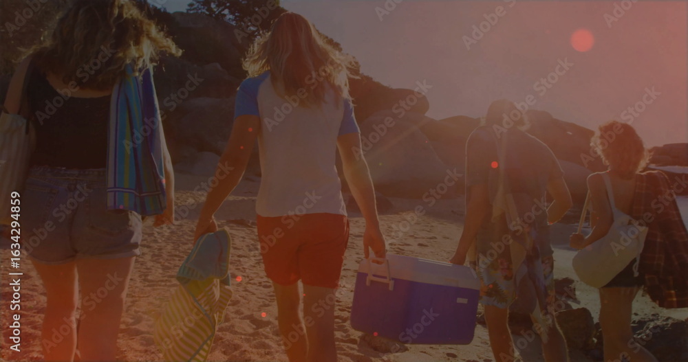 Naklejka premium Walking five friends carrying towels, bags and cooler along shoreline to boulders under sunlight