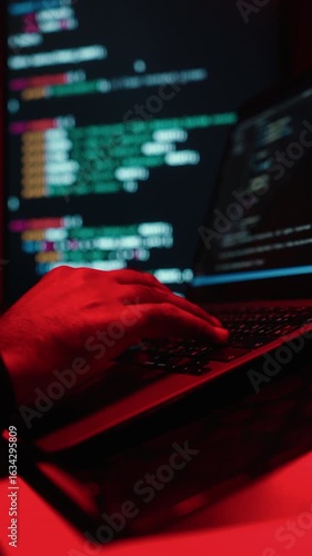 Close-up hand keyboard Hacker in balaclava with an obscured face is stealing data, representing cybercrime, hacking, dark web activity, and online security threats in red light. Cyber Security.
