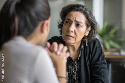 Mature Hispanic woman coaching a junior colleague on conflict resolution, demonstrating empathy and clear communication