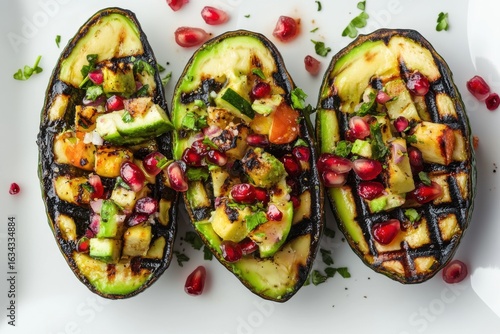 Grilled avocado halves topped with pomegranate seeds and herbs isolated on white background